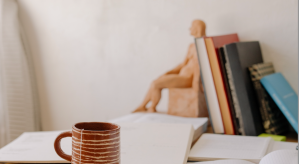 image of a tea cup on a desk with papers and books and clay figure of a non binary body
